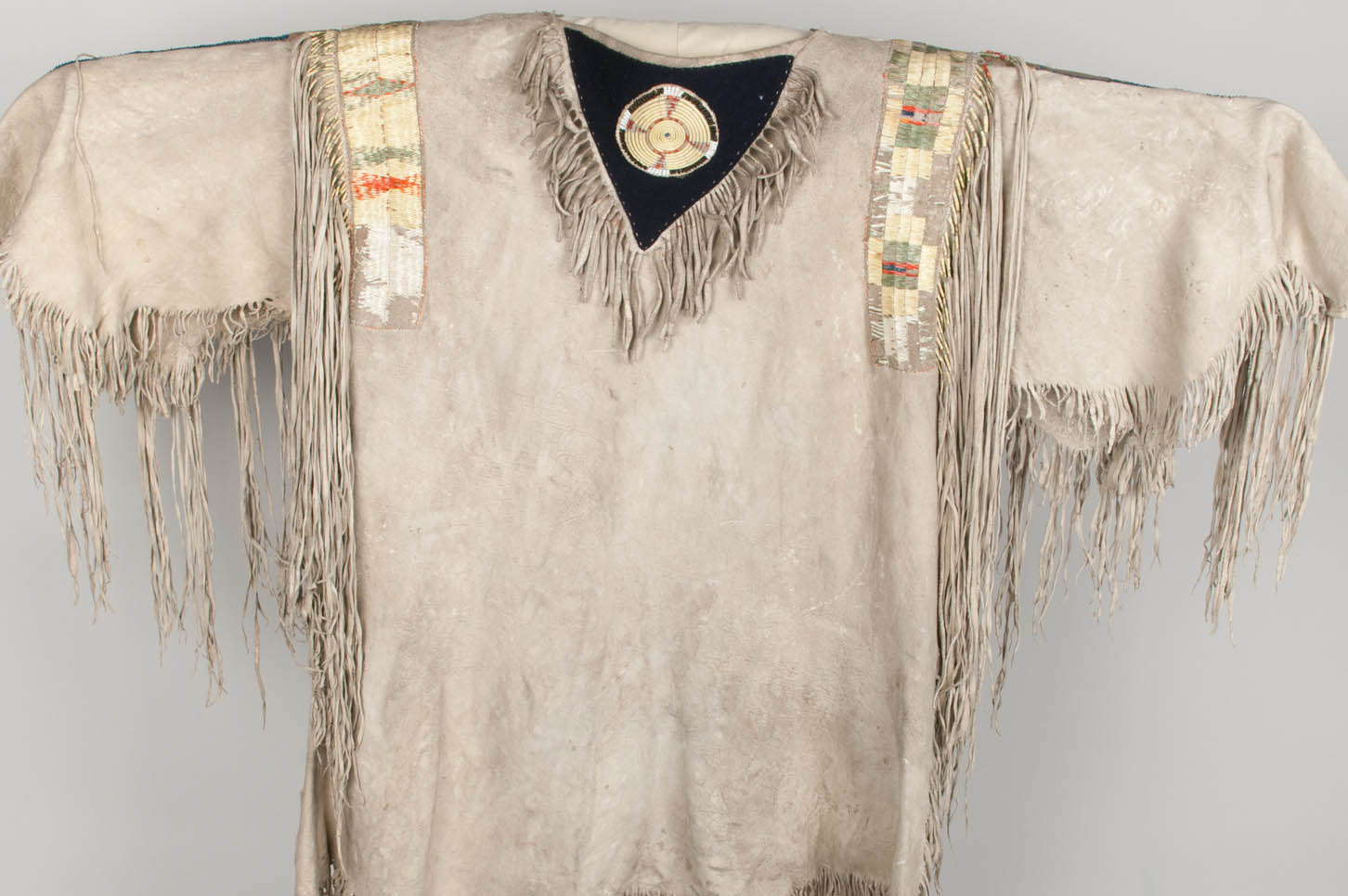 Men's ceremonial shirt, constructed out of at least 3 hides for the body of the shirt and more hides for the fringe. The neckflaps retain the original form of the animal's neck, which is decorated with a rosette of single bundle, quill-wrapped horsehair
